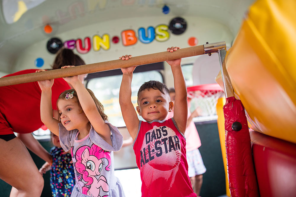 Kids swing energetically on monkeybars with FUN BUS's kids entertainment franchise.