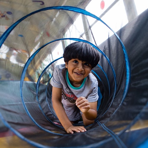 A girl crawling through a tube enjoys FUN BUS's kids indoor play franchise.