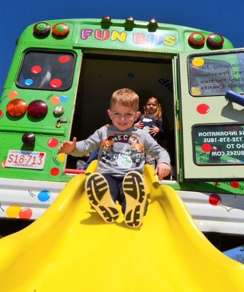 A happy little boy sliding down FUN BUS's bright yellow slide.